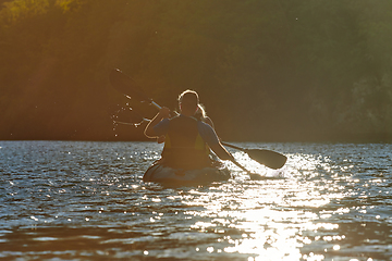 Image showing A young couple enjoying an idyllic kayak ride in the middle of a beautiful river surrounded by forest greenery in sunset time