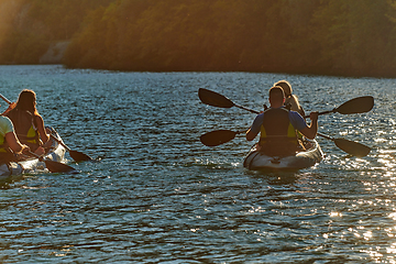 Image showing A group of friends enjoying fun and kayaking exploring the calm river, surrounding forest and large natural river canyons during an idyllic sunset.