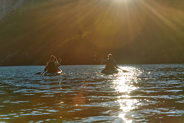 Image showing A group of friends enjoying fun and kayaking exploring the calm river, surrounding forest and large natural river canyons during an idyllic sunset.