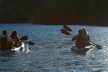 Image showing A group of friends enjoying fun and kayaking exploring the calm river, surrounding forest and large natural river canyons during an idyllic sunset.