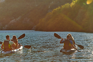 Image showing A group of friends enjoying fun and kayaking exploring the calm river, surrounding forest and large natural river canyons during an idyllic sunset.