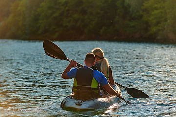 Image showing A young couple enjoying an idyllic kayak ride in the middle of a beautiful river surrounded by forest greenery in sunset time