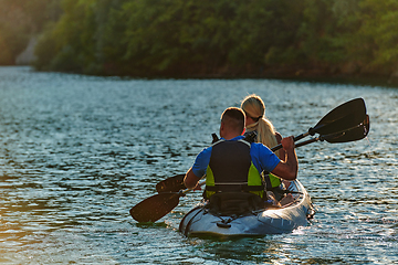 Image showing A young couple enjoying an idyllic kayak ride in the middle of a beautiful river surrounded by forest greenery in sunset time