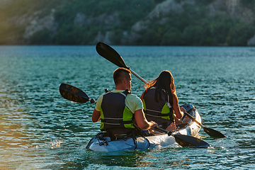 Image showing A young couple enjoying an idyllic kayak ride in the middle of a beautiful river surrounded by forest greenery in sunset time