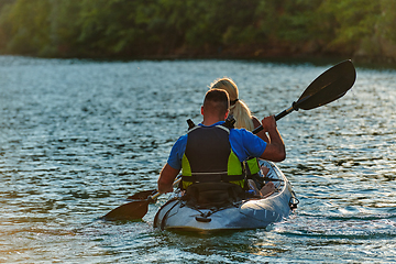 Image showing A young couple enjoying an idyllic kayak ride in the middle of a beautiful river surrounded by forest greenery in sunset time