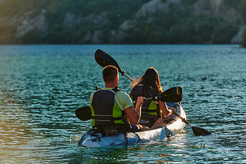 Image showing A young couple enjoying an idyllic kayak ride in the middle of a beautiful river surrounded by forest greenery in sunset time