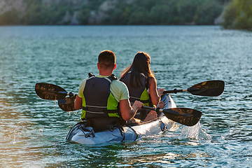 Image showing A young couple enjoying an idyllic kayak ride in the middle of a beautiful river surrounded by forest greenery in sunset time