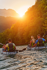 Image showing A group of friends enjoying fun and kayaking exploring the calm river, surrounding forest and large natural river canyons during an idyllic sunset.