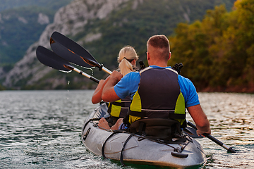 Image showing A young couple enjoying an idyllic kayak ride in the middle of a beautiful river surrounded by forest greenery in sunset time