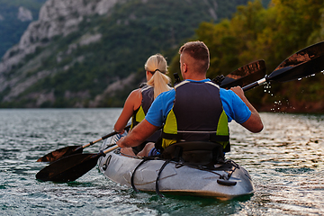 Image showing A young couple enjoying an idyllic kayak ride in the middle of a beautiful river surrounded by forest greenery in sunset time