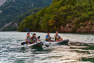 Image showing A group of friends enjoying having fun and kayaking while exploring the calm river, surrounding forest and large natural river canyons