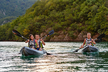 Image showing A group of friends enjoying fun and kayaking exploring the calm river, surrounding forest and large natural river canyons during an idyllic sunset.