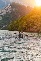 Image showing A young couple enjoying an idyllic kayak ride in the middle of a beautiful river surrounded by forest greenery in sunset time