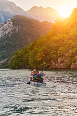 Image showing A young couple enjoying an idyllic kayak ride in the middle of a beautiful river surrounded by forest greenery in sunset time