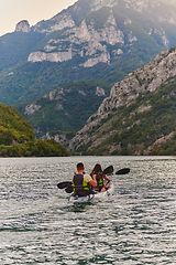 Image showing A young couple enjoying an idyllic kayak ride in the middle of a beautiful river surrounded by forest greenery in sunset time