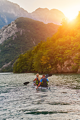 Image showing A young couple enjoying an idyllic kayak ride in the middle of a beautiful river surrounded by forest greenery in sunset time