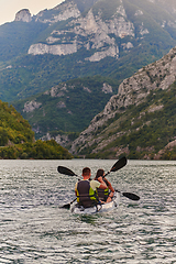 Image showing A young couple enjoying an idyllic kayak ride in the middle of a beautiful river surrounded by forest greenery in sunset time