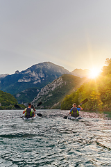 Image showing A group of friends enjoying fun and kayaking exploring the calm river, surrounding forest and large natural river canyons during an idyllic sunset.