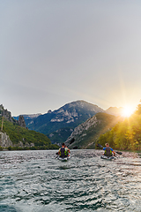 Image showing A group of friends enjoying fun and kayaking exploring the calm river, surrounding forest and large natural river canyons during an idyllic sunset.