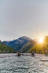 Image showing A group of friends enjoying fun and kayaking exploring the calm river, surrounding forest and large natural river canyons during an idyllic sunset.