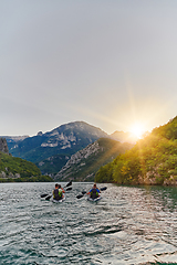 Image showing A group of friends enjoying fun and kayaking exploring the calm river, surrounding forest and large natural river canyons during an idyllic sunset.