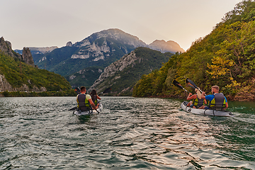 Image showing A group of friends enjoying fun and kayaking exploring the calm river, surrounding forest and large natural river canyons during an idyllic sunset.