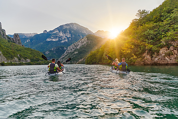 Image showing A group of friends enjoying fun and kayaking exploring the calm river, surrounding forest and large natural river canyons during an idyllic sunset.