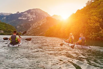 Image showing A group of friends enjoying fun and kayaking exploring the calm river, surrounding forest and large natural river canyons during an idyllic sunset.