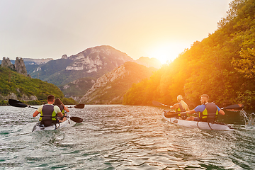 Image showing A group of friends enjoying fun and kayaking exploring the calm river, surrounding forest and large natural river canyons during an idyllic sunset.