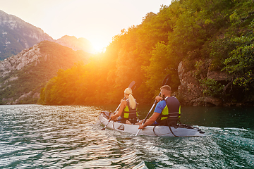 Image showing A group of friends enjoying fun and kayaking exploring the calm river, surrounding forest and large natural river canyons during an idyllic sunset.