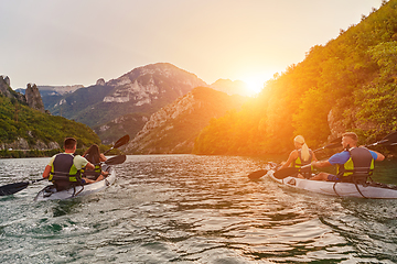 Image showing A group of friends enjoying fun and kayaking exploring the calm river, surrounding forest and large natural river canyons during an idyllic sunset.