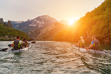 Image showing A group of friends enjoying fun and kayaking exploring the calm river, surrounding forest and large natural river canyons during an idyllic sunset.