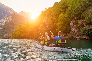 Image showing A group of friends enjoying fun and kayaking exploring the calm river, surrounding forest and large natural river canyons during an idyllic sunset.