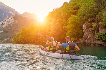 Image showing A group of friends enjoying fun and kayaking exploring the calm river, surrounding forest and large natural river canyons during an idyllic sunset.