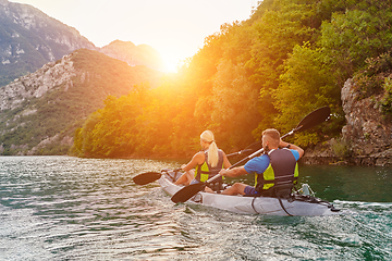 Image showing A group of friends enjoying fun and kayaking exploring the calm river, surrounding forest and large natural river canyons during an idyllic sunset.