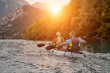 Image showing A group of friends enjoying fun and kayaking exploring the calm river, surrounding forest and large natural river canyons during an idyllic sunset.