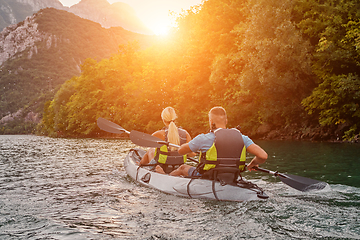 Image showing A group of friends enjoying fun and kayaking exploring the calm river, surrounding forest and large natural river canyons during an idyllic sunset.