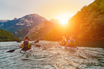 Image showing A group of friends enjoying fun and kayaking exploring the calm river, surrounding forest and large natural river canyons during an idyllic sunset.