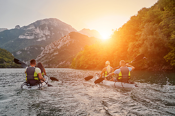 Image showing A group of friends enjoying fun and kayaking exploring the calm river, surrounding forest and large natural river canyons during an idyllic sunset.