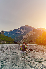 Image showing A young couple enjoying an idyllic kayak ride in the middle of a beautiful river surrounded by forest greenery in sunset time