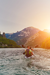 Image showing A young couple enjoying an idyllic kayak ride in the middle of a beautiful river surrounded by forest greenery in sunset time