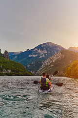 Image showing A young couple enjoying an idyllic kayak ride in the middle of a beautiful river surrounded by forest greenery in sunset time