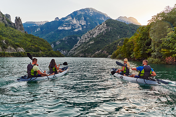 Image showing A group of friends enjoying fun and kayaking exploring the calm river, surrounding forest and large natural river canyons during an idyllic sunset.