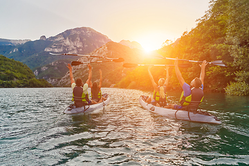 Image showing A group of friends enjoying fun and kayaking exploring the calm river, surrounding forest and large natural river canyons during an idyllic sunset.