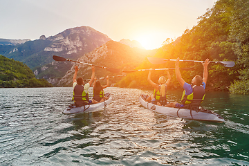 Image showing A group of friends enjoying fun and kayaking exploring the calm river, surrounding forest and large natural river canyons during an idyllic sunset.