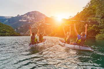 Image showing A group of friends enjoying fun and kayaking exploring the calm river, surrounding forest and large natural river canyons during an idyllic sunset.