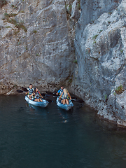 Image showing A group of friends enjoying fun and kayaking exploring the calm river, surrounding forest and large natural river canyons during an idyllic sunset.