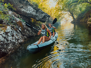 Image showing A young couple enjoying an idyllic kayak ride in the middle of a beautiful river surrounded by forest greenery