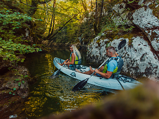 Image showing A young couple enjoying an idyllic kayak ride in the middle of a beautiful river surrounded by forest greenery