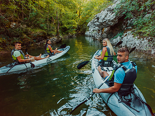 Image showing A group of friends enjoying having fun and kayaking while exploring the calm river, surrounding forest and large natural river canyons